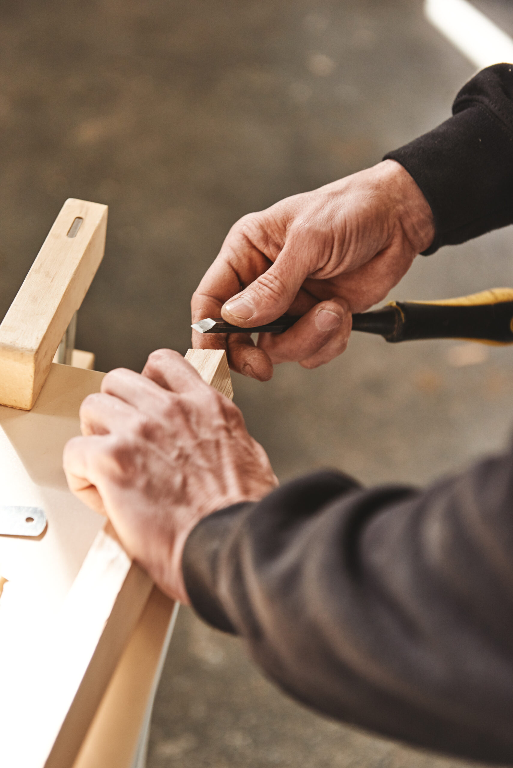 Custom woodworking and carpentry. Close up of a carpenter's hands holding wooden plank and chisel menuiserie sur-mesure